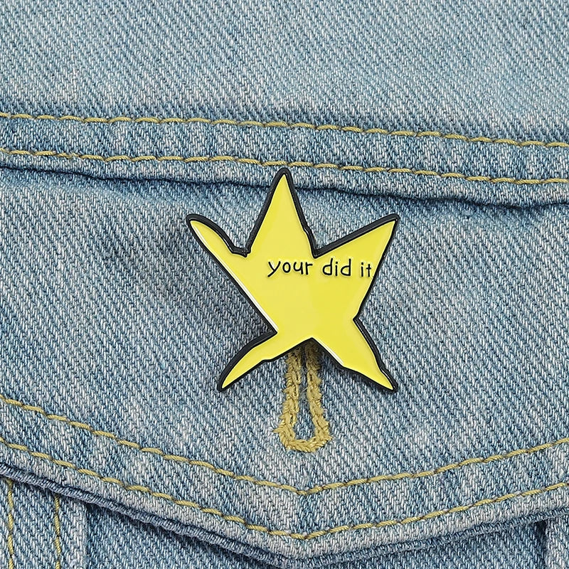 A yellow star enamel pin with the text your did it on a denim fabric.