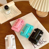 A collection of pink and teal adjustable foldable phone and tablet stands resting on a white paper next to a notebook.