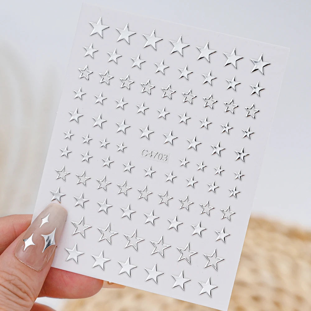 A hand holds a sheet of metallic 3D star nail art stickers for crafting or decoration.