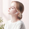 A light-skinned woman wearing white clothing and listening to music with a white wired earphone.