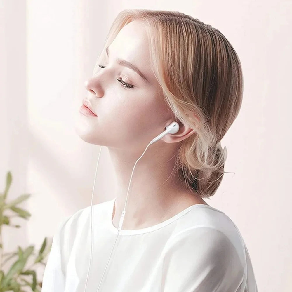 A light-skinned woman wearing white clothing and listening to music with a white wired earphone.