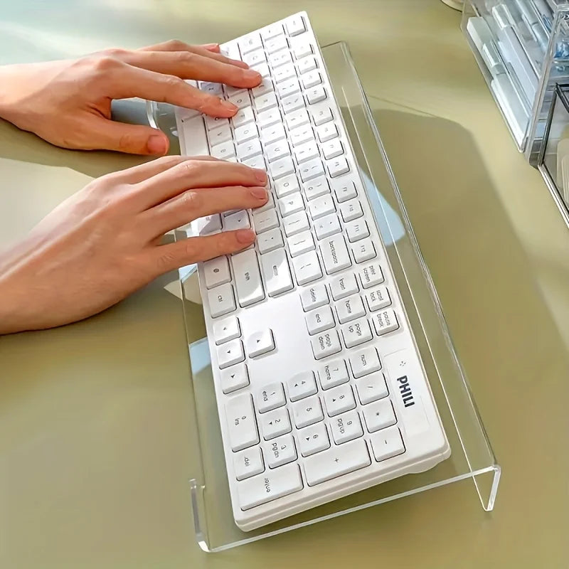 A white keyboard is placed in a clear acrylic stand on a light green desk surface.