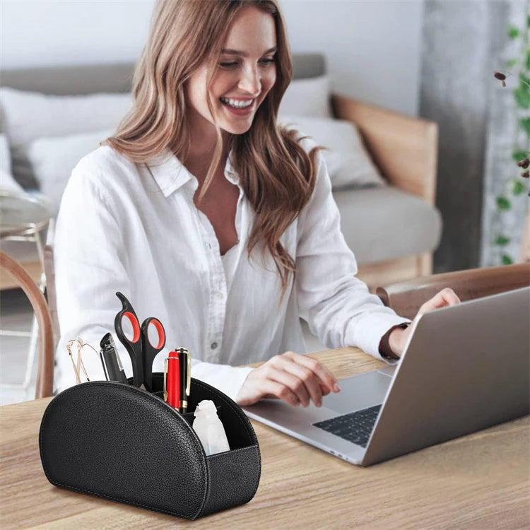 A woman is smiling while working on a laptop next to a black PU leather remote control holder with five compartments.