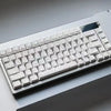 A close-up view of a white mechanical keyboard with side-lit cherry profile keycaps resting on a white surface.