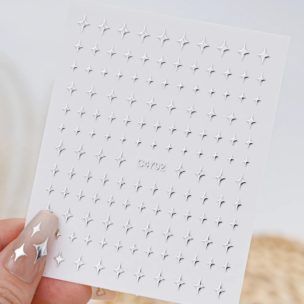 A hand holds a sheet of metallic 3D star nail art stickers for crafting or decoration.