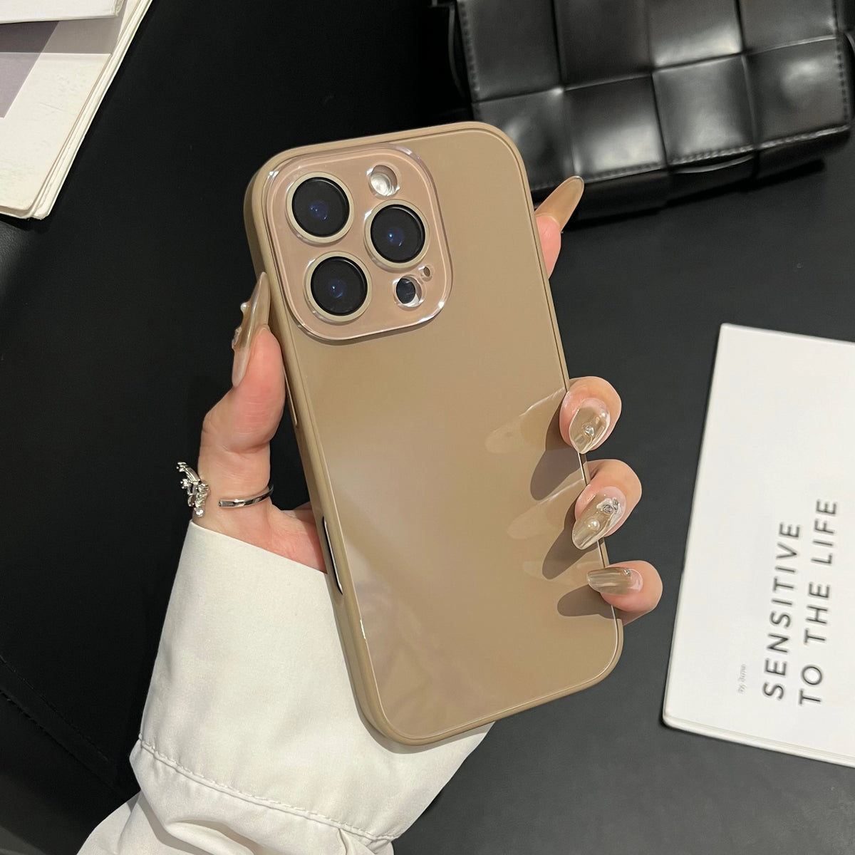 A hand holds a beige iPhone with a clear glossy tempered glass shockproof case against a dark background.