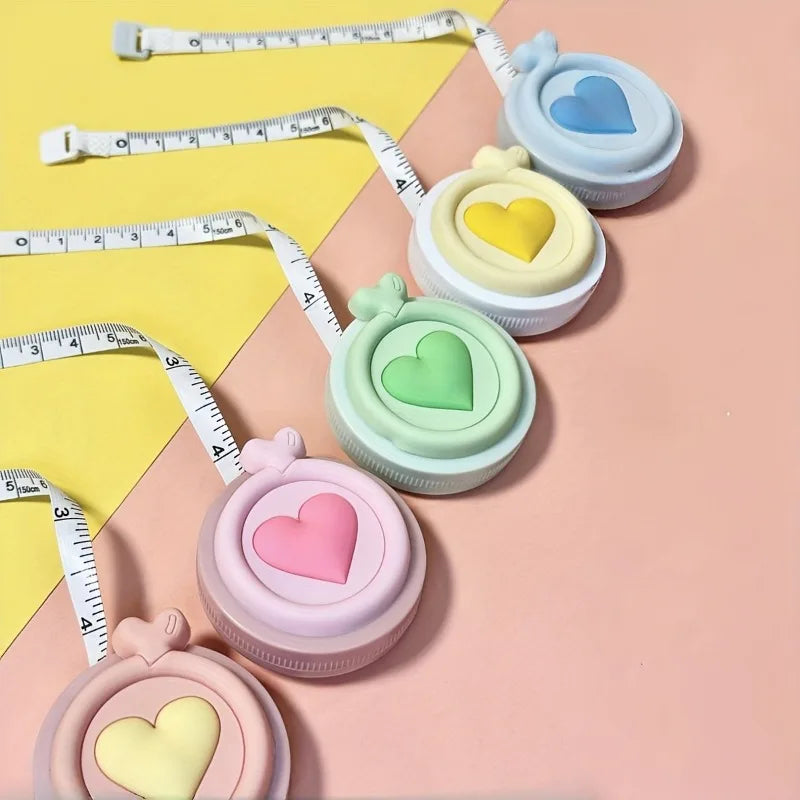Colección de cintas métricas en forma de corazón y retráctiles, en varios colores pastel como azul, amarillo y rosa.
