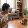 A woman is using an interactive pet training pen to interact with a cat on the floor.