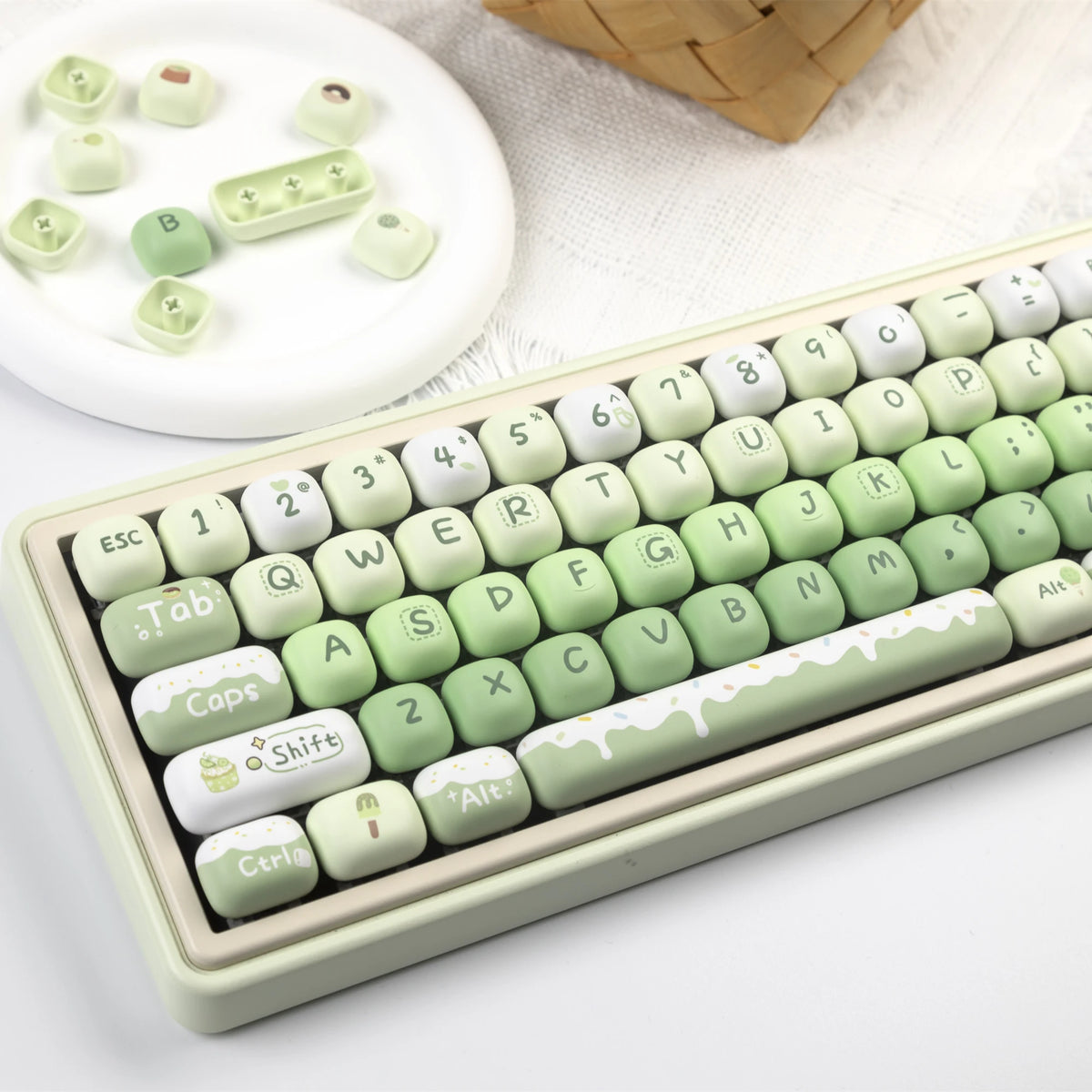 A close-up view of a light green PBT keycap set with various characters and symbols, displayed next to a woven basket.