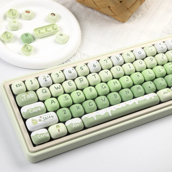 A close-up view of a light green PBT keycap set with various characters and symbols, displayed next to a woven basket.
