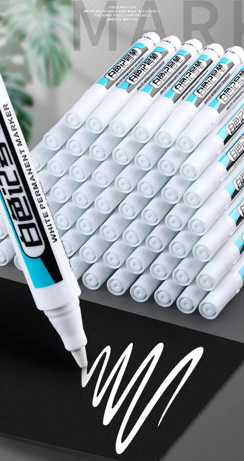 A close-up view of a large pack of white permanent paint marker pens with blue accents, showing the tip writing on black pape