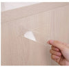 A hand is peeling a piece of clear double-sided nano adhesive tape from a light wood cabinet surface.