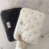 A white quilted padded laptop sleeve case is shown next to a black one, resting on a white surface.