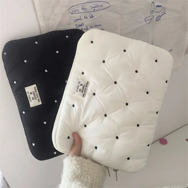 A white quilted padded laptop sleeve case is shown next to a black one, resting on a white surface.