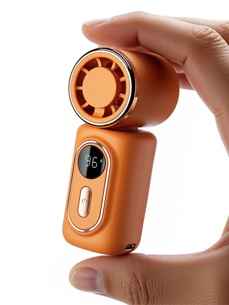 A hand holds an orange portable rechargeable handheld cooling fan with a circular grille on top.