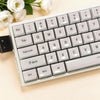 A close-up view of a white mechanical keyboard with light gray keycaps and a floral arrangement in the background.