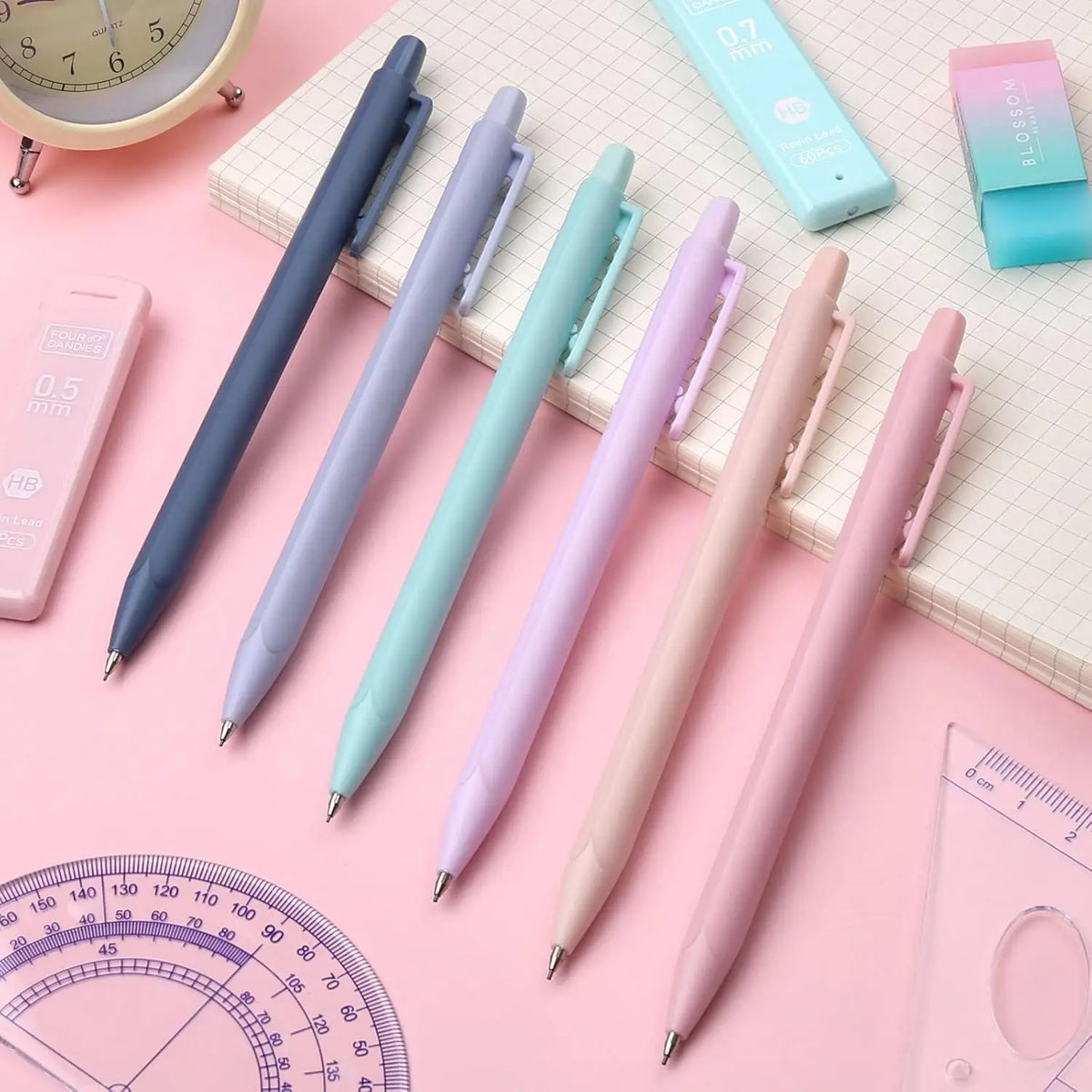 A set of aesthetic pastel mechanical pencils in various shades of blue, green, and pink resting on a pink surface.