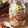 A glass jar filled with Mary's lentil salad, featuring grains, vegetables, and tomato sauce.
