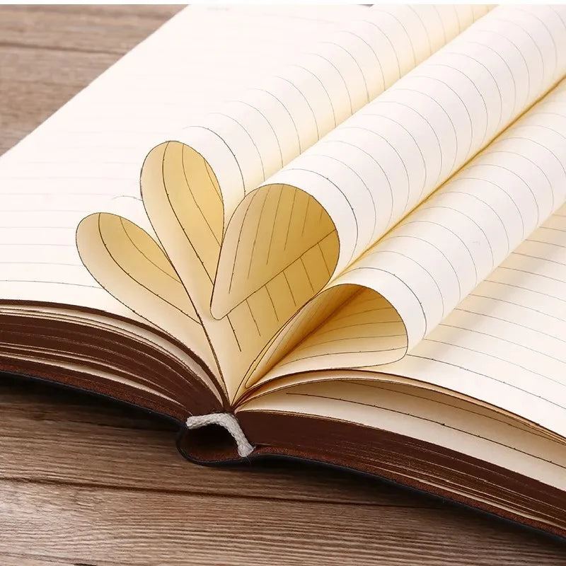 An open notebook with lined pages and a decorative leaf design on the cover, resting on a wooden surface.