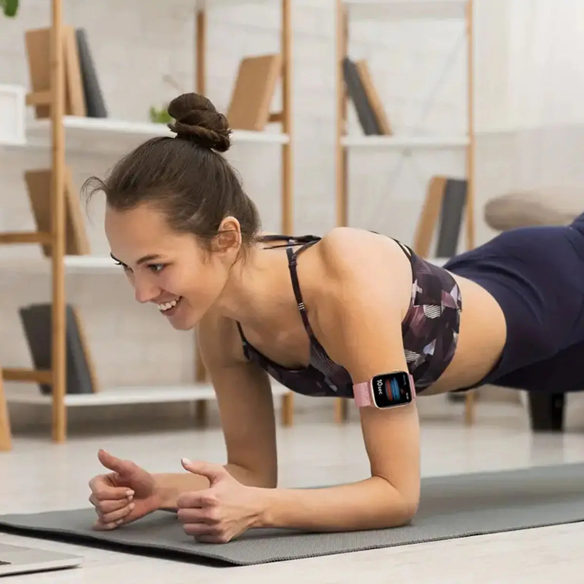 A woman is performing a stretch or exercise on a mat, wearing a dark athletic top and a black smartwatch.
