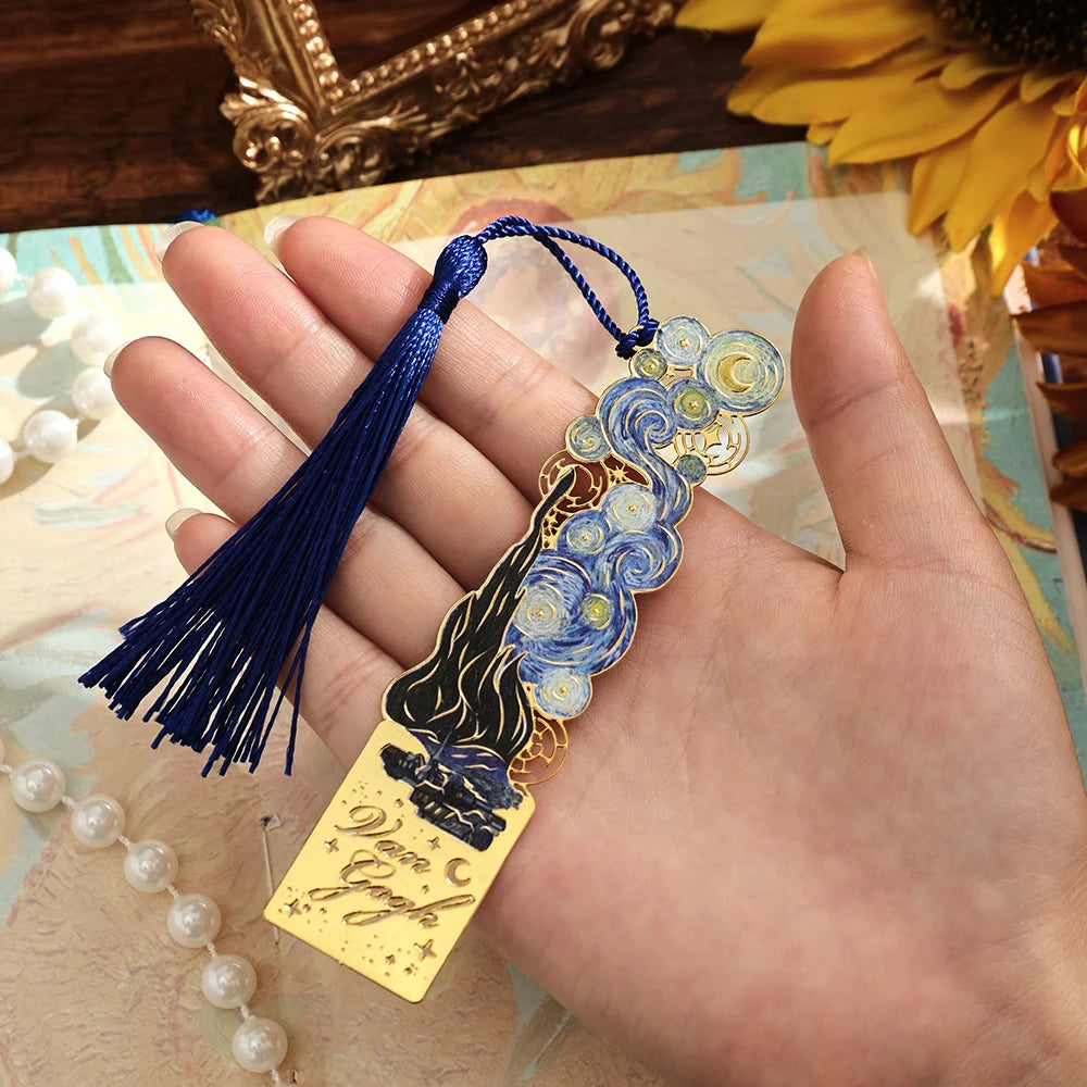 A hand holds a vintage artistic metal bookmark with a blue and gold design and a dark blue tassel.