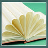 An open premium A5 leather journal showing cream-colored pages and a reddish-brown cover on a green surface.