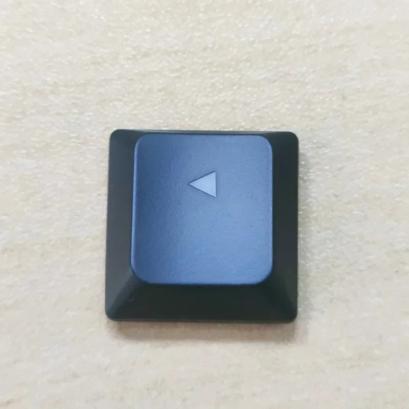 A close-up view of a dark blue replacement keycap with a triangular arrow marker for a Dell Alienware keyboard.