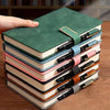 A stack of A5 retro leather notebooks in various shades of green, pink, and beige on a wooden surface.