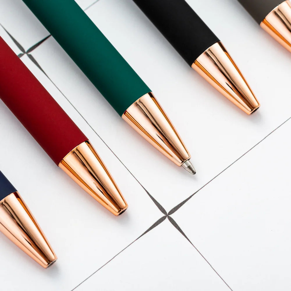 A close-up view of three retractable pens with gold accents lying on a white grid surface.