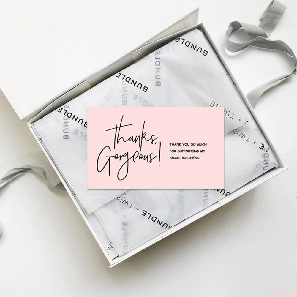 A square package of thank you cards with a pink message inside, resting on a white surface.