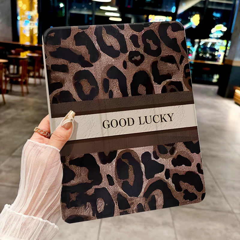 A hand holds a leopard print protective case for an iPad, featuring a brown and black pattern with the text GOOD LUCKY.