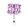 A glitter acrylic badge reel with the text IT IS WHAT IT IS in purple script.