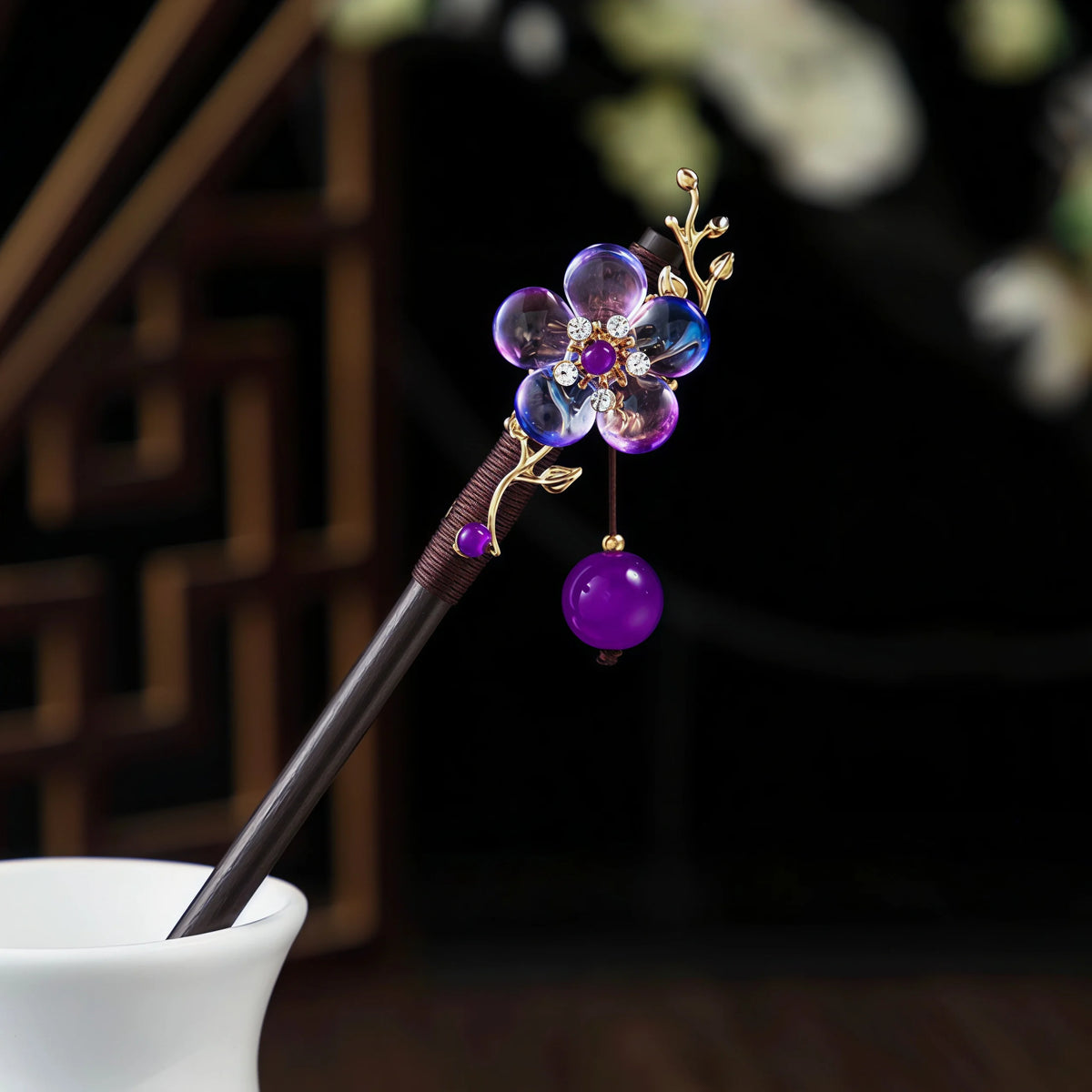 Une épingle à cheveux avec un bâton en bois foncé et un accessoire floral violet orné de fleurs en verre et d'accents dorés.