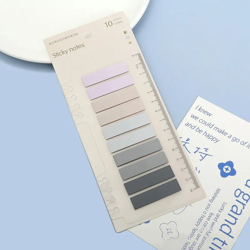 A sheet of transparent self-adhesive sticky notes in various pastel and gray shades is shown on a light blue background.