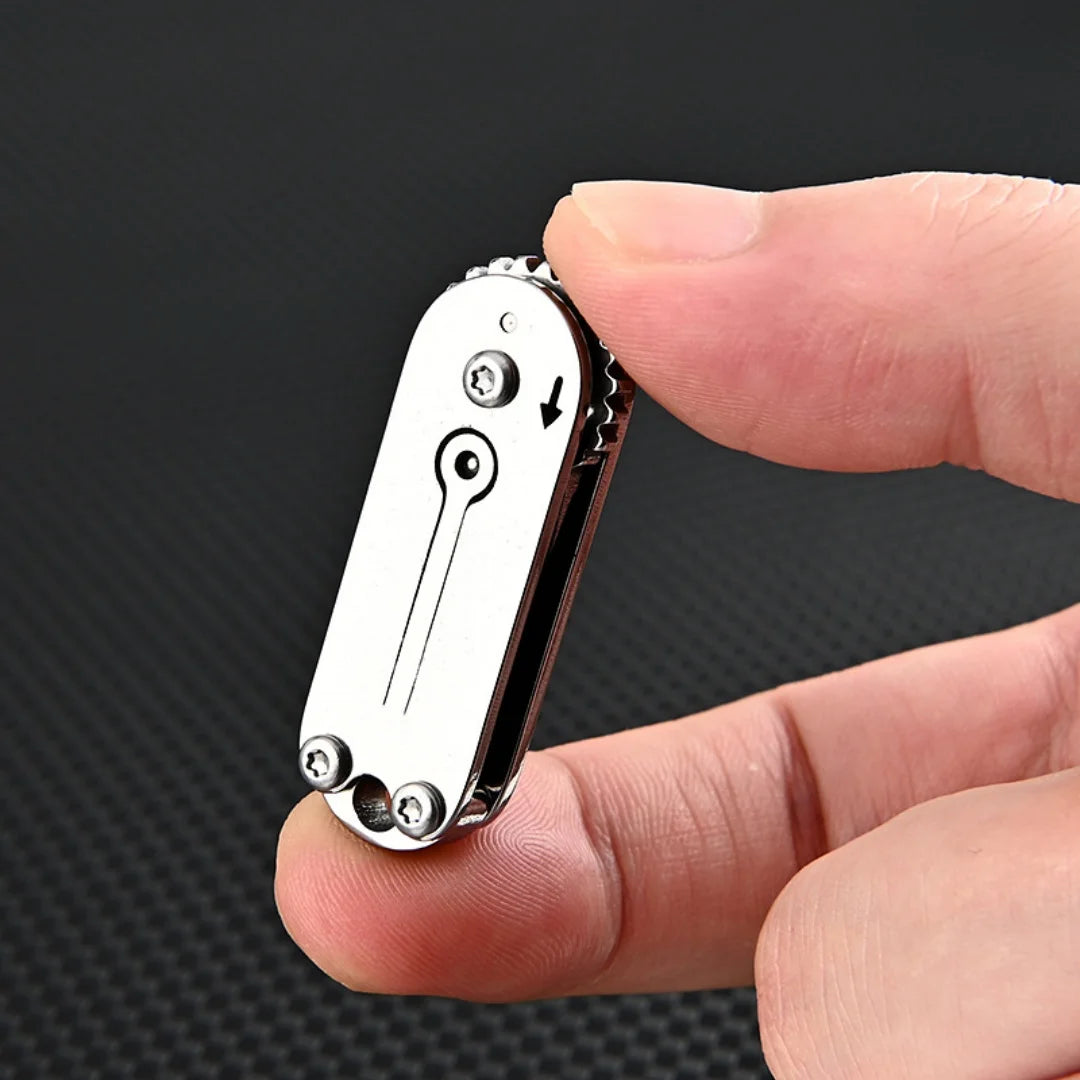 A hand holds a compact stainless steel pocket knife with a keychain attachment against a dark background.