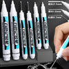A collection of white permanent paint marker pens in various sizes and tips are shown being held by a hand.