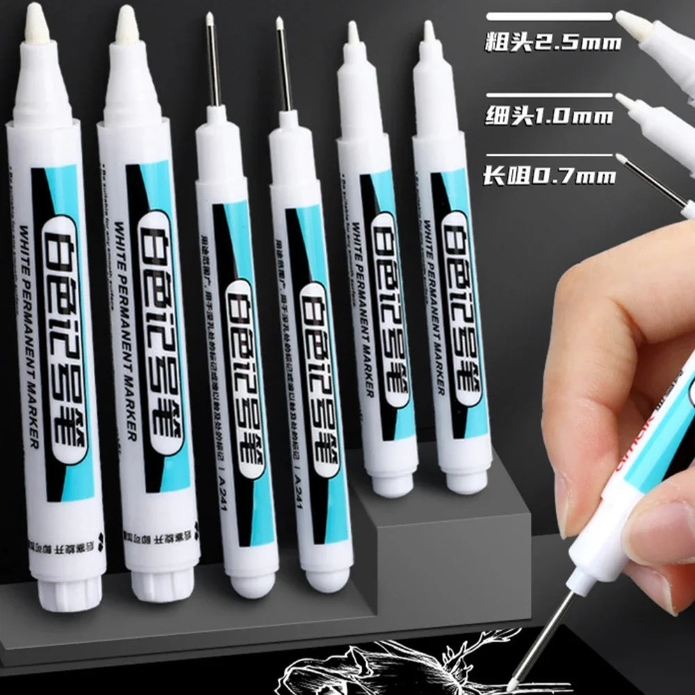 A collection of white permanent paint marker pens in various sizes and tips are shown being held by a hand.