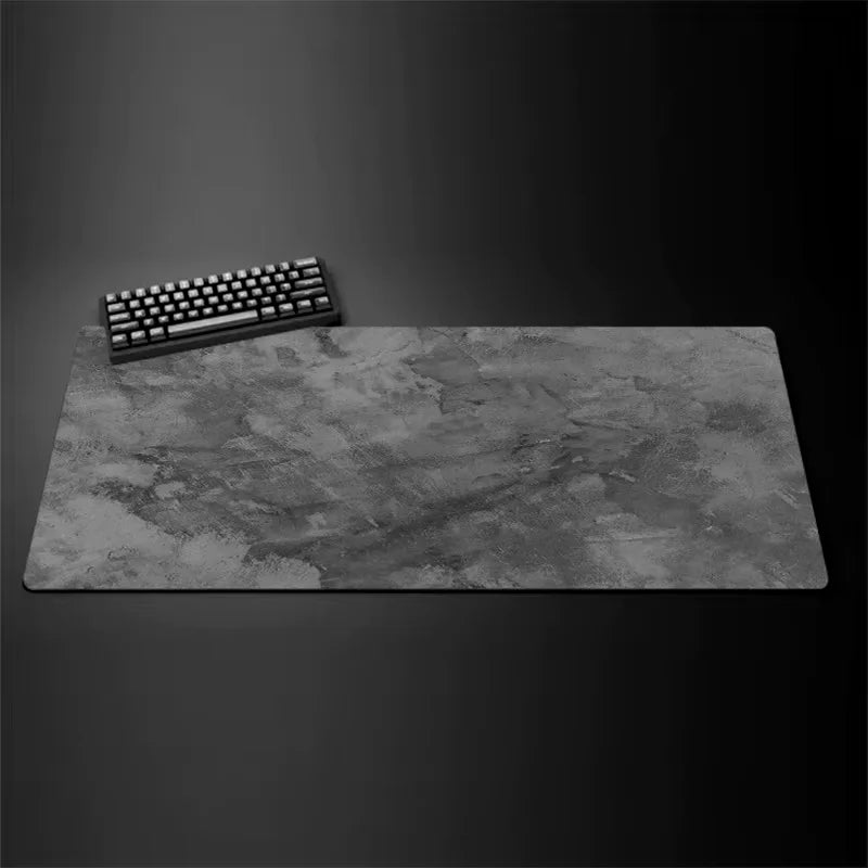 A gray overlocked mouse pad is shown next to a black computer keyboard on a dark surface.