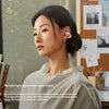A woman wearing white SHOKZ Bluetooth headphones in a casual setting.