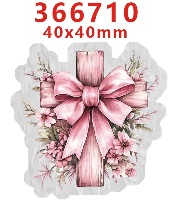 A pink wooden cross with a bow surrounded by floral greenery and leaves.