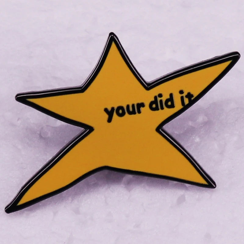 A yellow star shaped enamel pin with the text your did it on a white surface.