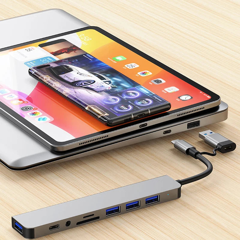 A silver laptop is shown with a Multi-Port USB-C Hub Adapter connected to a smartphone and a USB cable.