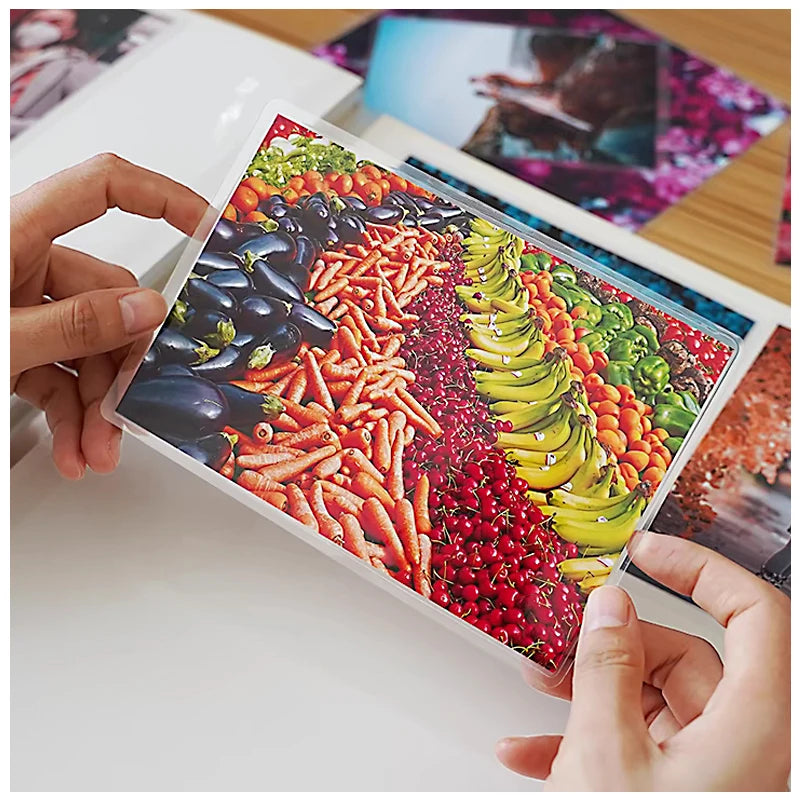 A hand holds a clear thermal laminating pouch filled with colorful vegetables like peppers, carrots, and corn.