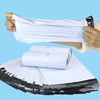 Hands holding a stack of white waterproof packaging bags next to a pile of black and white paper.
