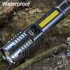 A silver tactical LED flashlight with a yellow lens is shown in a wet, outdoor environment.
