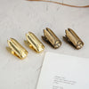 A set of gold-toned metal beetle binder clips lying on a white surface next to a piece of paper.