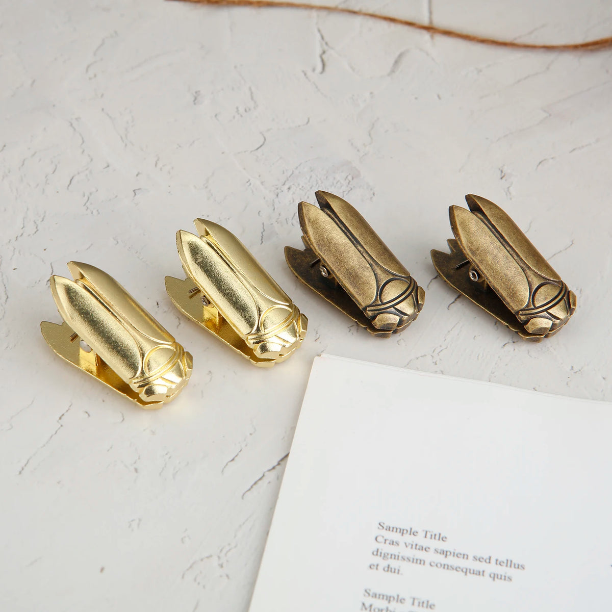 A set of gold-toned metal beetle binder clips lying on a white surface next to a piece of paper.