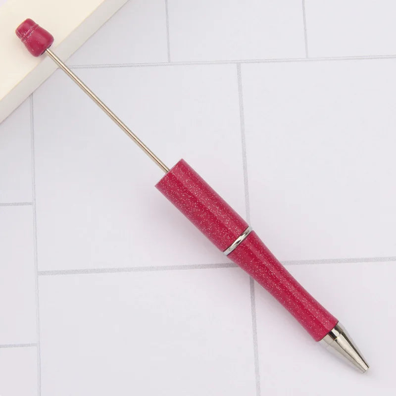 A pink DIY beadable pen with a silver band and a black ink tip resting on a white surface.