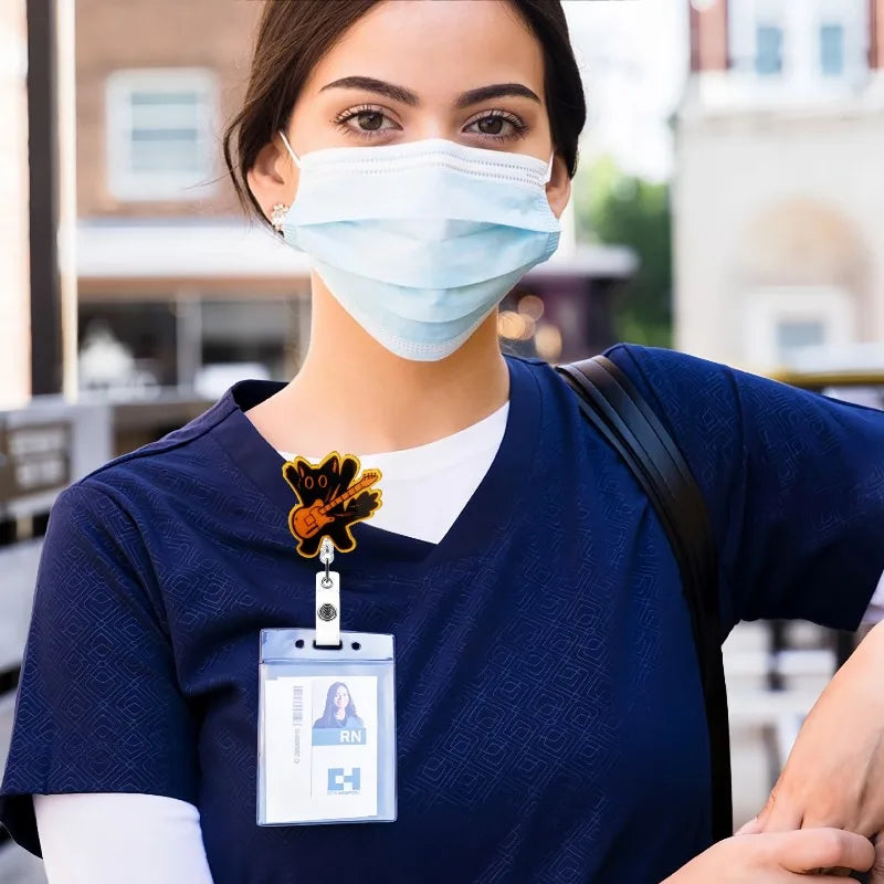 A woman wearing a blue scrubs shirt and a light blue face mask holds an acrylic nurse badge reel.