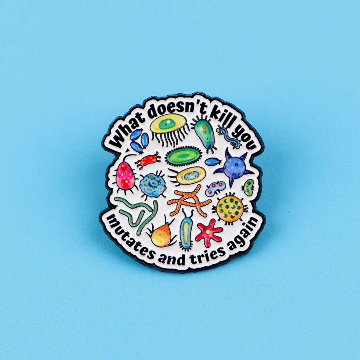 An enamel pin featuring various stylized microorganisms and the text What doesn't kill you mates and tries again